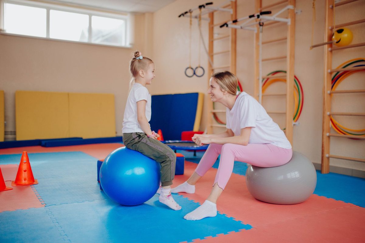 Fisioterapia pediátrica en Barcelona: niña sentada en una pelota de ejercicio con su fisioterapeuta en la sala de tratamiento