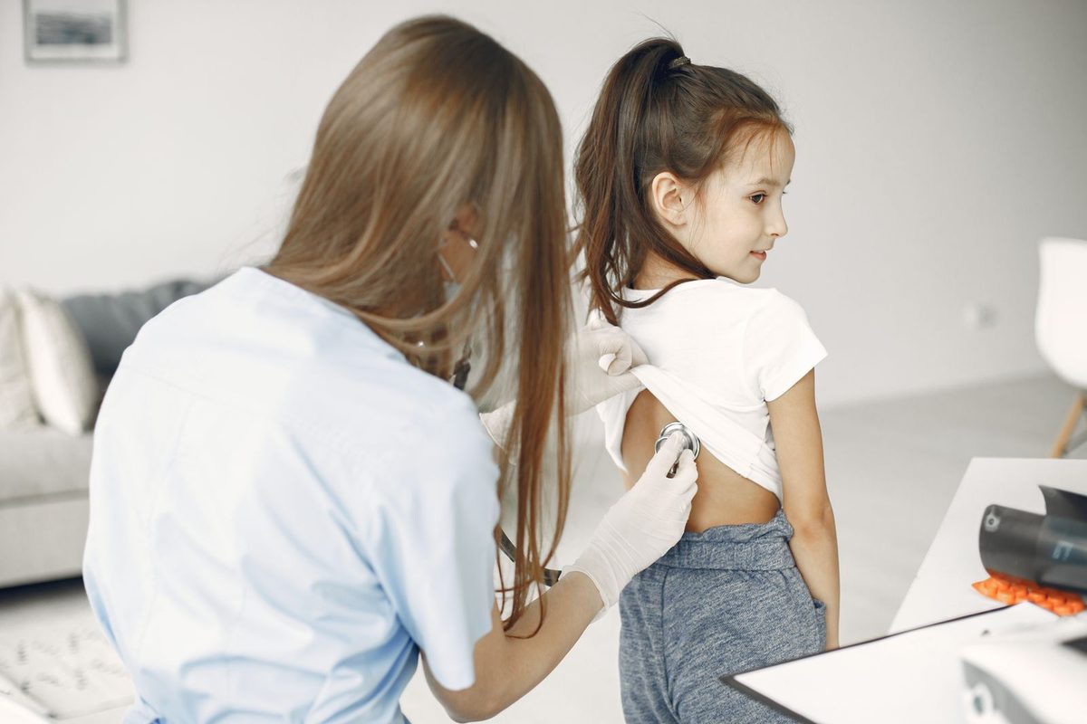 Fisioterapia respiratoria pediátrica en Barcelona: fisioterapeuta auscultando la espalda de una niña en la consulta